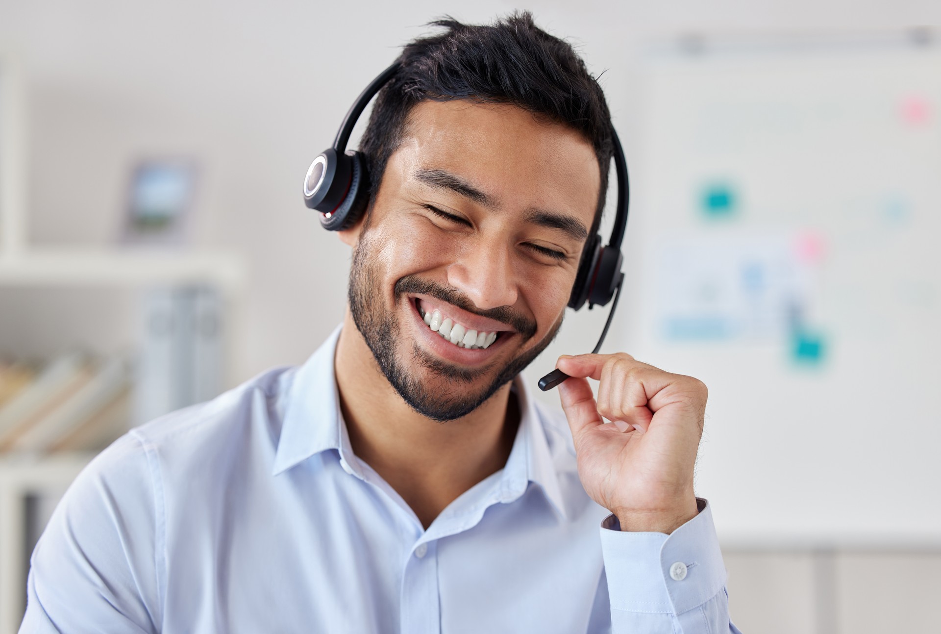 Face of happy mixed race call centre telemarketing agent with big smile talking on headset while working in office. Confident friendly businessman operating helpdesk for customer service sales support